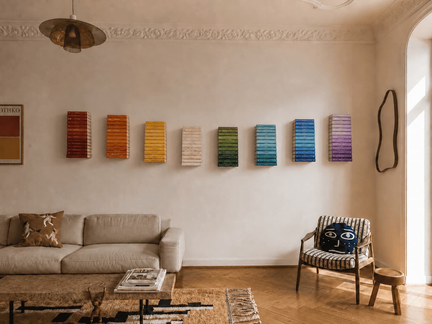 Mur de salon avec des étagères murales composant une bibliothèque arc-en-ciel, organisée par blocs rouges, orange, jaunes, blancs, verts, bleus et violets.