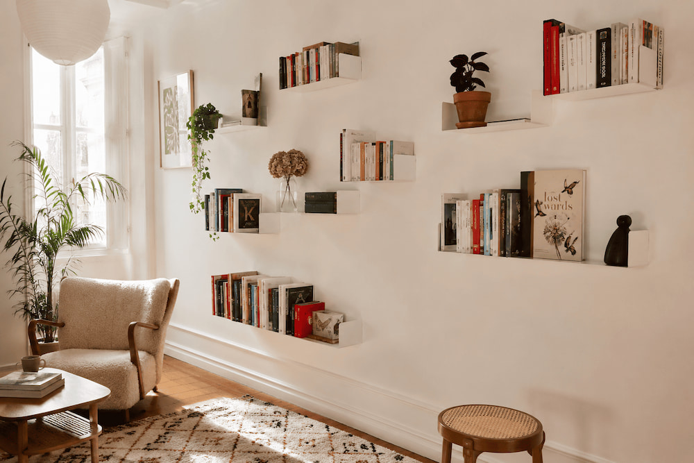 Salon lumineux avec huit étagères murales blanches de tailles variées disposées à différentes hauteurs en composition asymétrique.