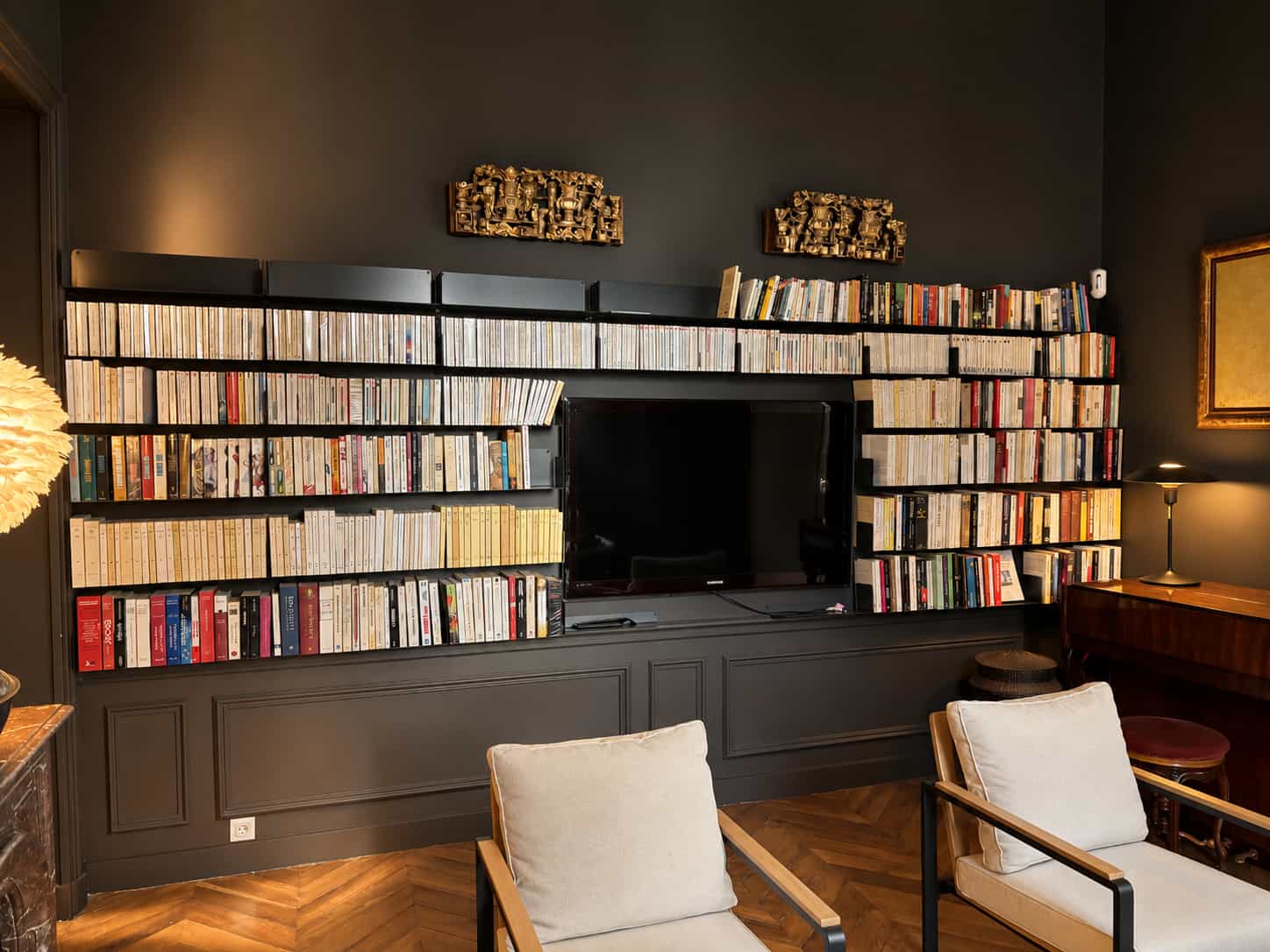 Bibliothèque murale grise sur mur anthracite, avec une palette de couleurs sombres harmonisée dans le salon