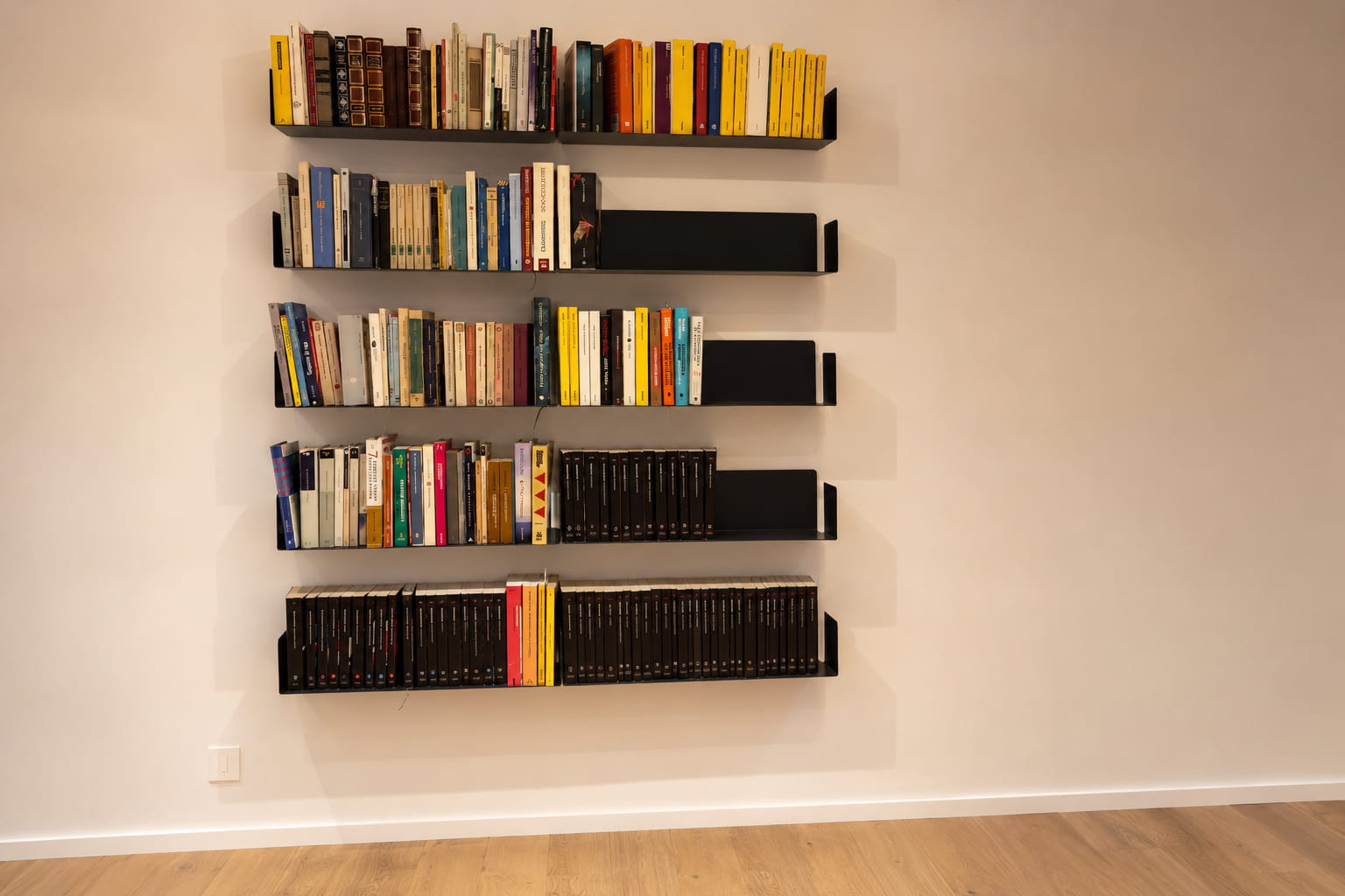 Bibliothèque murale noire avec livres colorés sur mur clair, créant un contraste équilibré dans la décoration intérieure