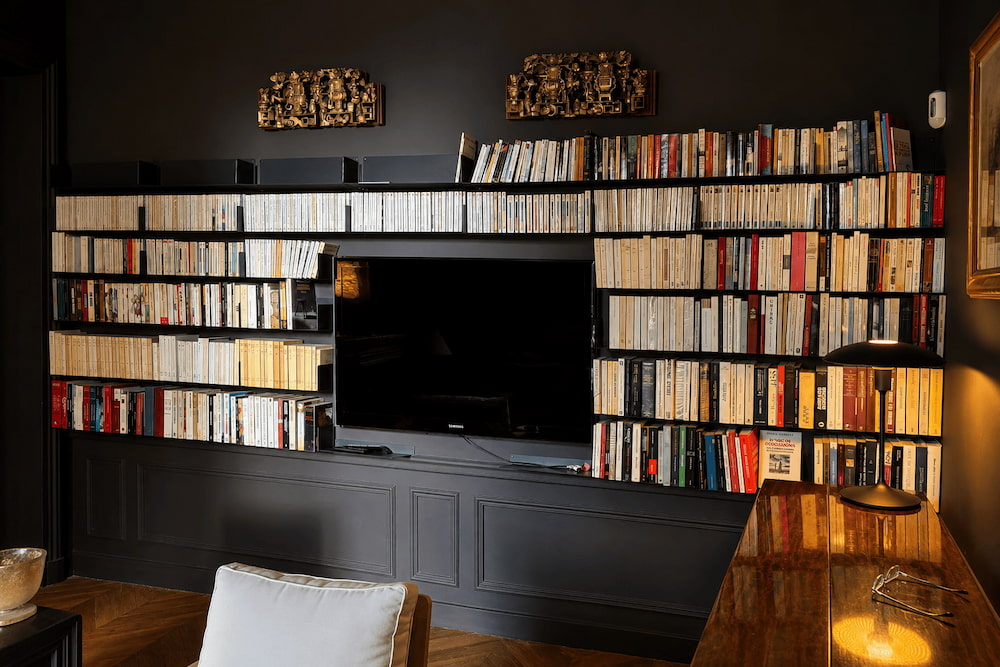 Bibliothèque murale pleine hauteur noire avec de longues étagères remplies de livres autour d’un téléviseur dans un salon spacieux.