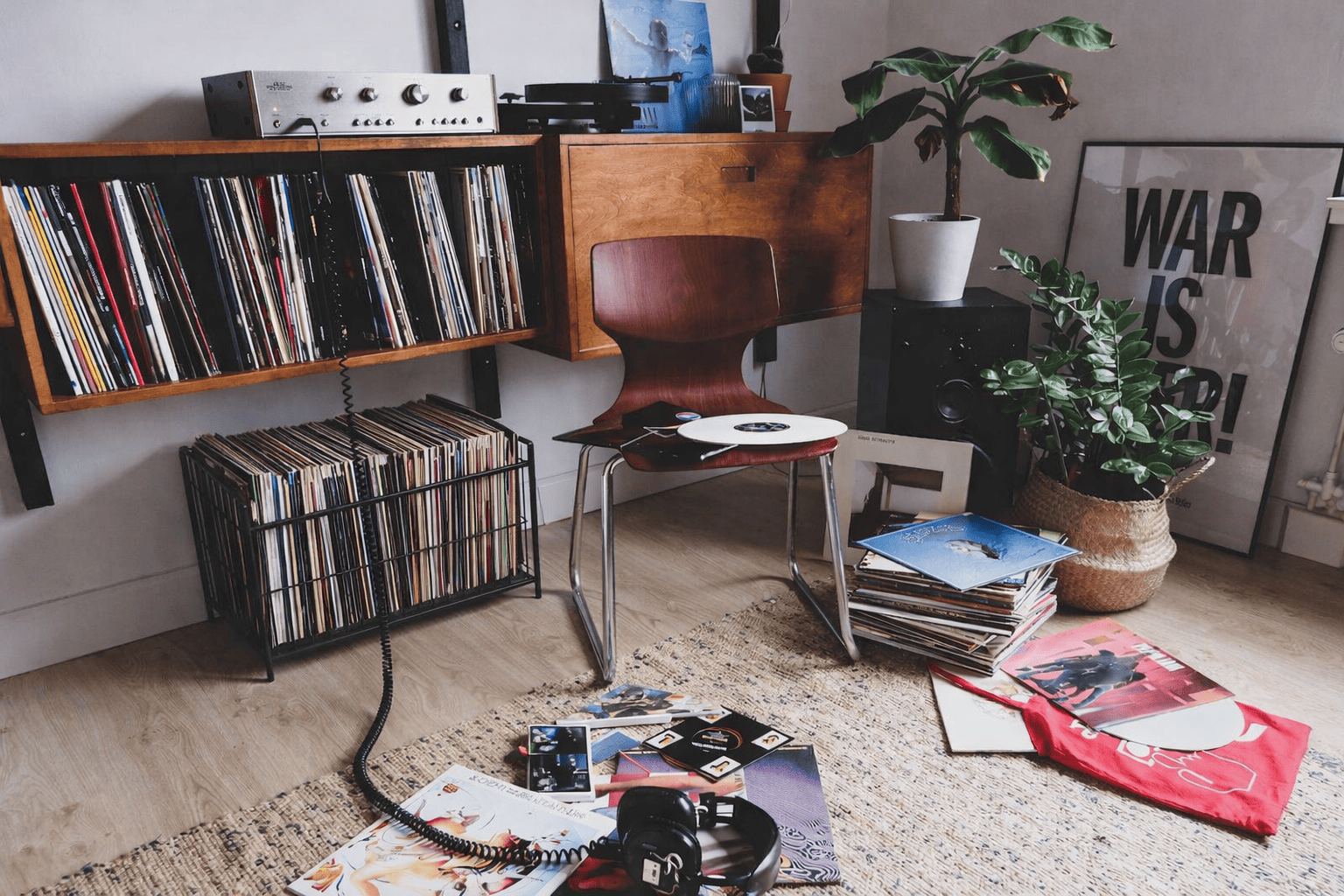 Boîte de rangement vinyle en métal sous un meuble vinyle mural en bois, dans un salon avec platine, fauteuil et pochettes de disques éparpillées