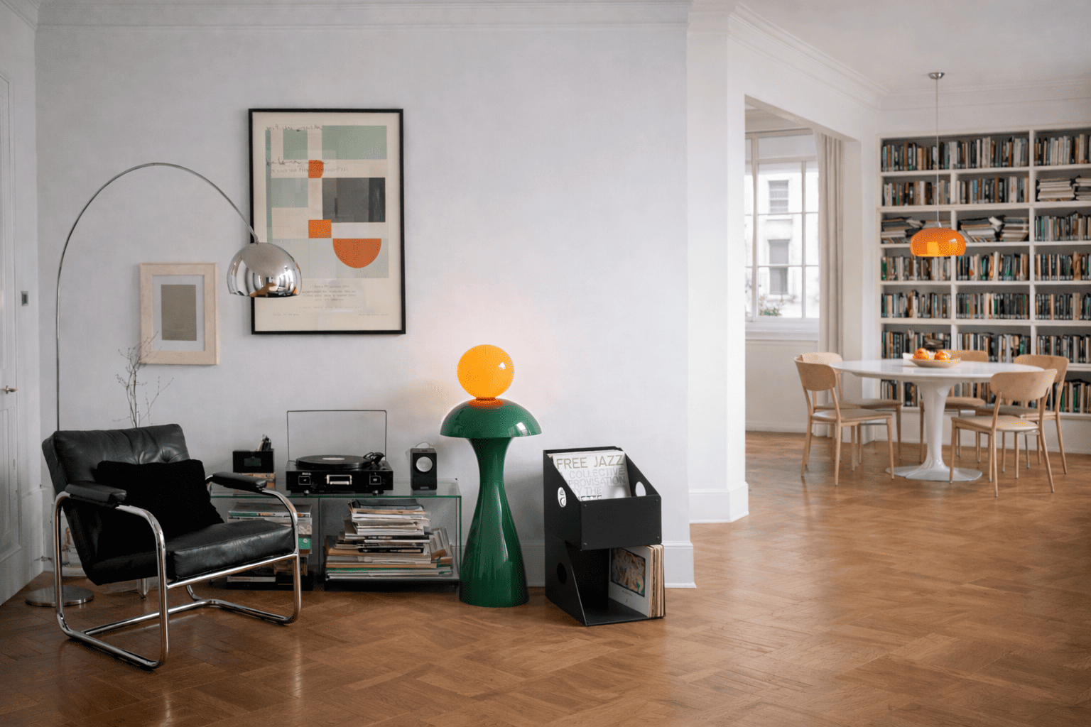 Boîte de rangement vinyle noire posée au sol à côté d’une lampe verte lumineuse dans un salon moderne, avec fauteuil en cuir, platine vinyle et disques empilés, ambiance calme et lumineuse avec parquet en bois et bibliothèque en arrière-plan