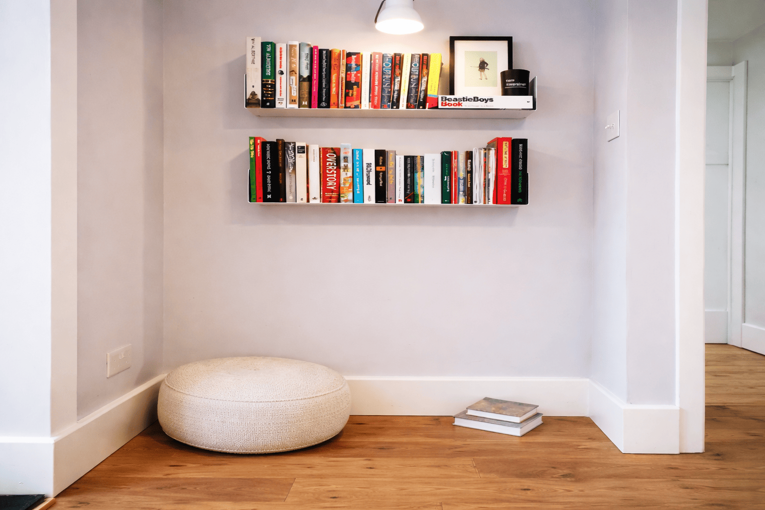 Étagères murales à livres installées dans un angle de pièce, créant un coin lecture minimaliste avec pouf et livres, mettant en avant une étagère pour livre compacte et décorative.