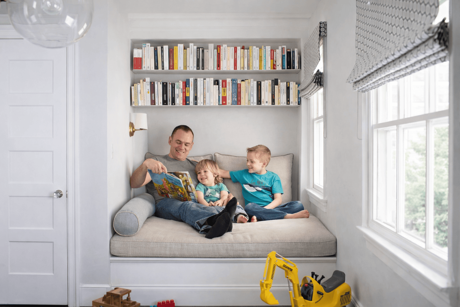 Étagère pour livre murale installée au-dessus d’un coin lecture familial, avec banquette et coussins, montrant des étagères murales à livres pratiques et esthétiques dans un espace de vie convivial.