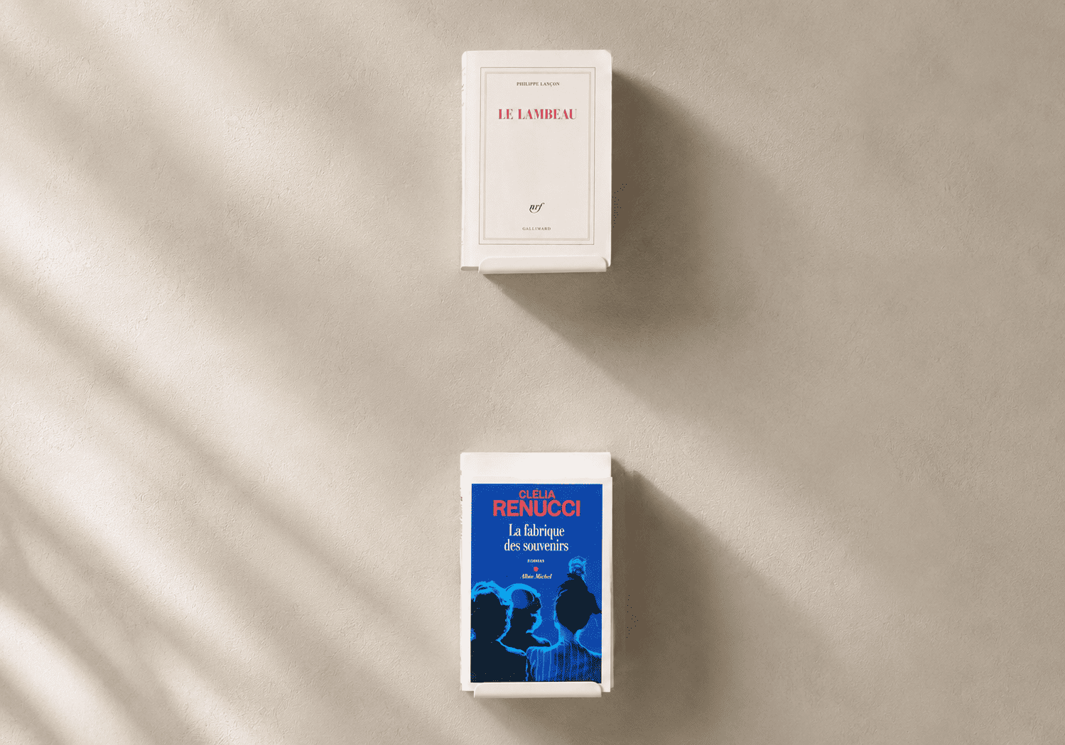 Deux étagères murales blanches à fixation invisible présentent chacune un livre sur un mur clair et minimaliste.