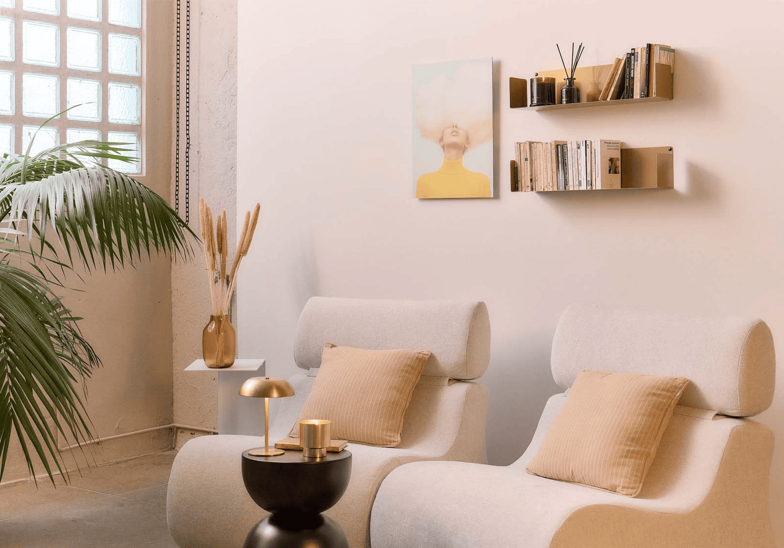 Étagères avec équerre invisible en métal or antique fixées sur un mur rose pâle, avec livres et diffuseur décoratif au-dessus de deux fauteuils blancs, dans un salon lumineux avec grande plante verte, coussins beiges et touches dorées.