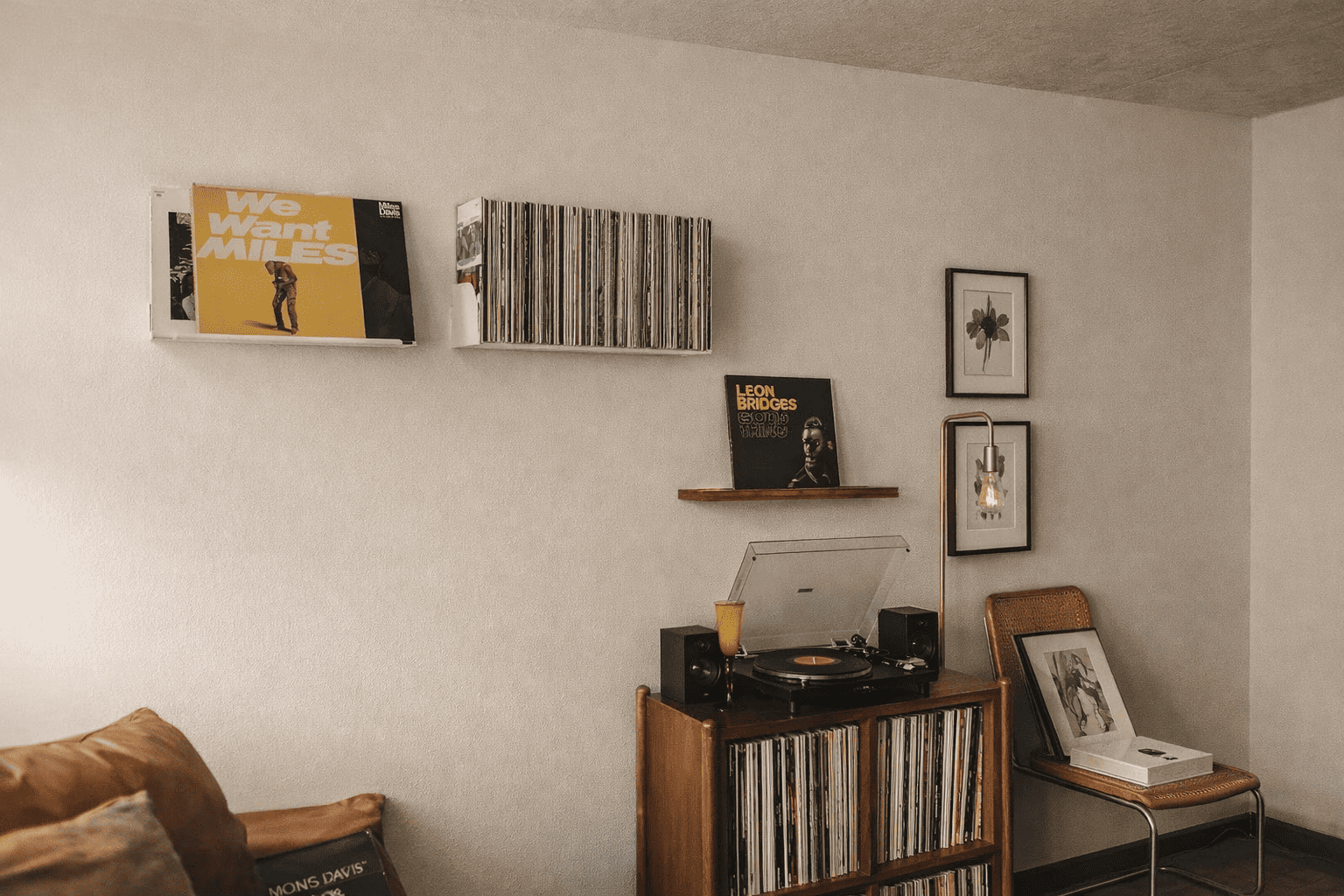 Étagère vinyle murale dans un salon chaleureux, au-dessus d’un meuble tourne-disque en bois, avec cadres botaniques, lampe sur pied dorée et collection de disques vinyles soigneusement exposée.