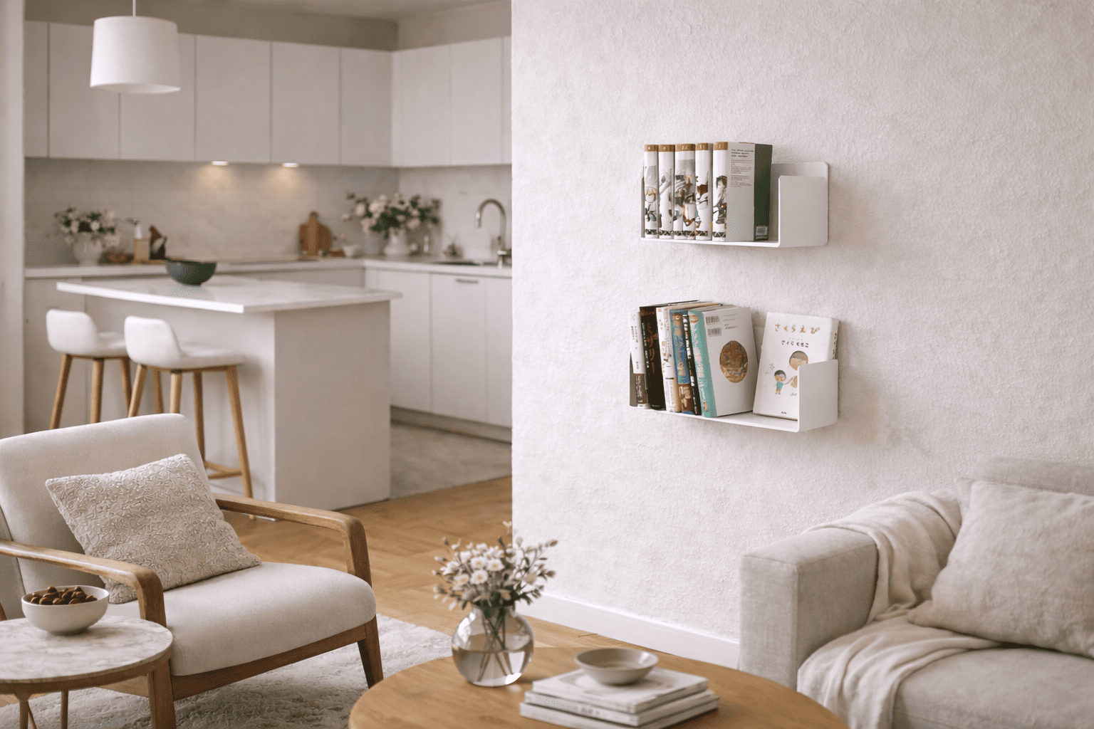 Petites étagères flottantes blanches fixées sur un mur texturé, avec livres et albums illustrés dans un salon clair ouvert sur une cuisine moderne, entouré de fauteuils, canapé beige et décoration douce.
