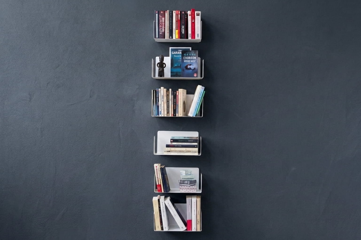 Six petites étagères murales blanches sont disposées verticalement sur un mur bleu foncé, avec des livres rangés debout, couchés et présentés de face.