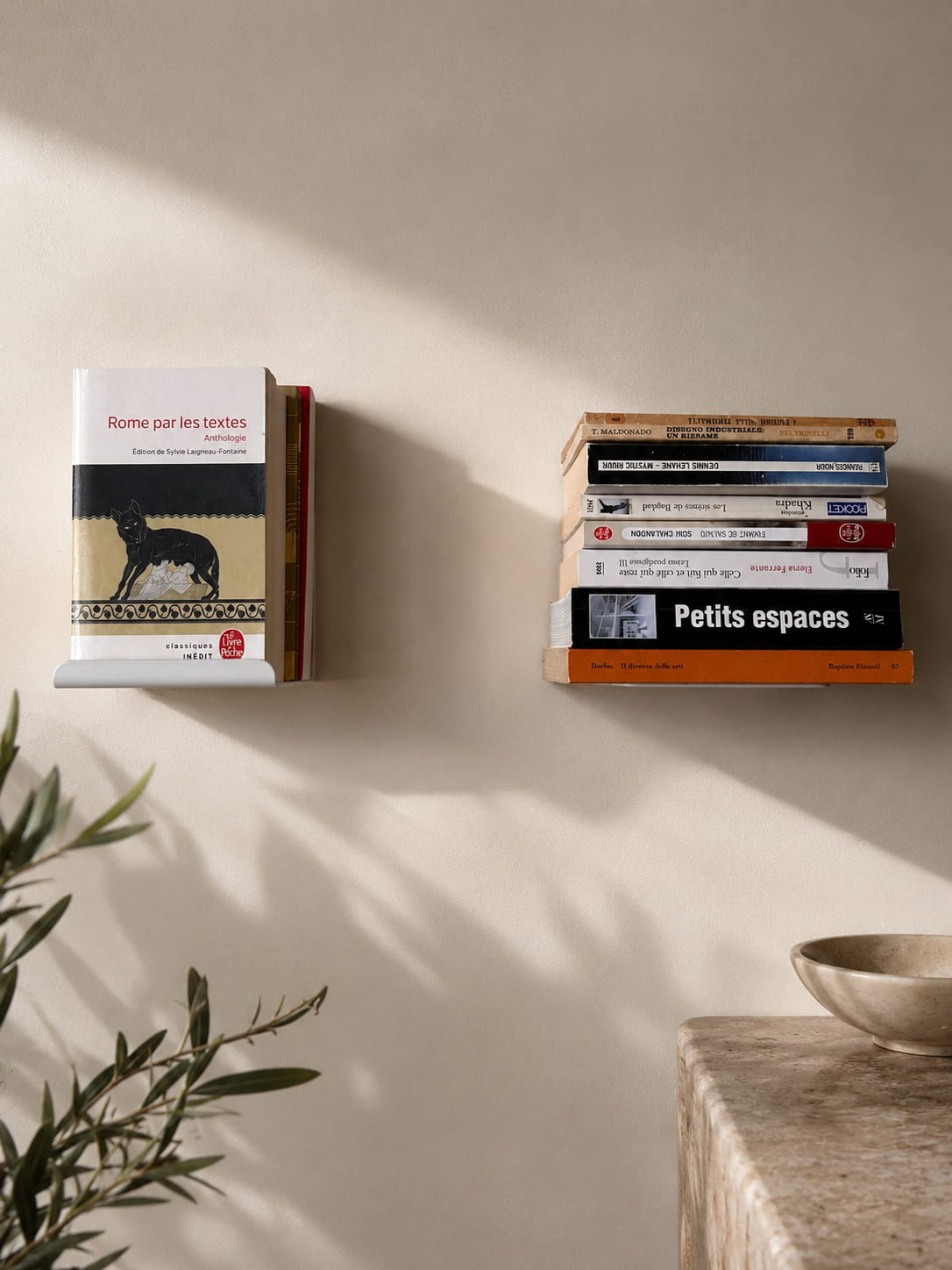 Petites étagères murales au design original sur un mur clair : l’une présente un livre de face, tandis que l’autre supporte une pile de livres horizontale.