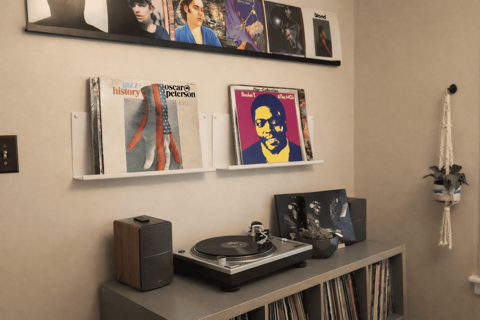 Présentoir vinyle mural minimaliste dans un salon moderne, avec deux étagères blanches exposant des pochettes de disques au-dessus d’un meuble platine et rangement vinyles.