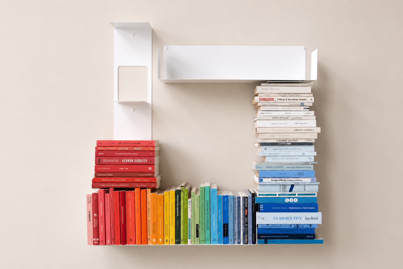 Livres rangés par couleur de tranche sur des étagères murales blanches, du rouge et orange vers le jaune, le vert, le bleu et les tons neutres.
