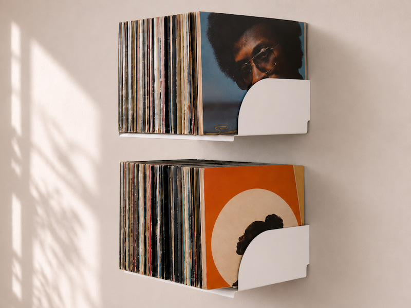 Deux étagères murales blanches avec des vinyles 33 tours rangés verticalement au-dessus d’une platine, une solution pour ranger ses vinyles tout en libérant de l’espace au sol.