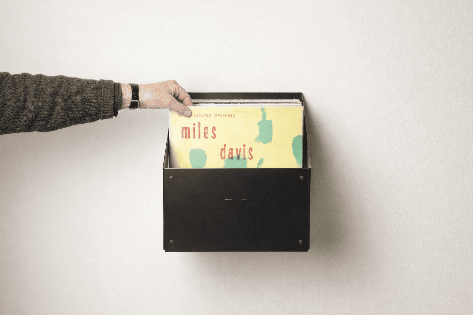 Bac mural noir de rangement vinyle 33 tours fixé au mur, avec une main qui range un disque vinyle, design minimaliste et épuré.