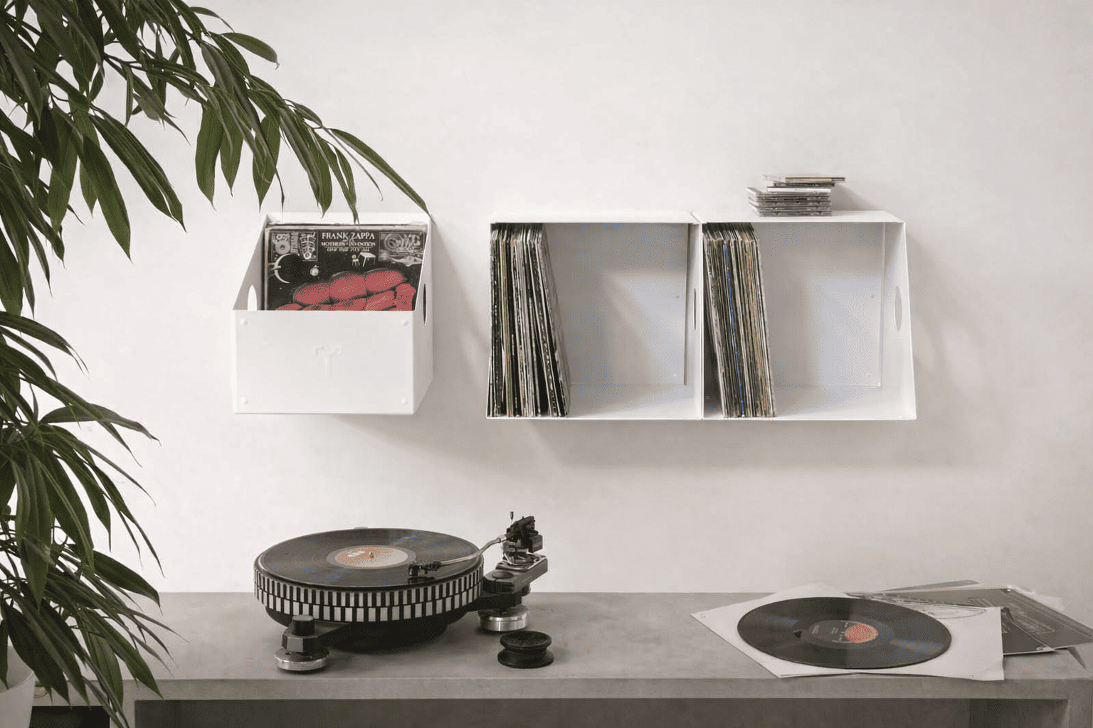 Ensemble de bacs muraux blancs de rangement vinyle 33 tours contenant plusieurs collections de disques, au-dessus d’une platine vinyle dans un intérieur lumineux.