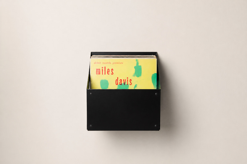 Collection de disques vinyles rangée verticalement dans un bac mural noir, avec les pochettes droites, soutenues et faciles à feuilleter.