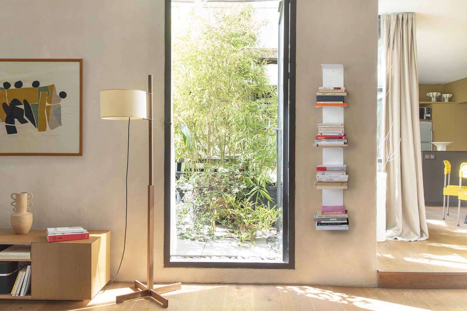 Bibliothèque murale blanche design dans un salon lumineux, avec étagères verticales remplies de livres – idée déco moderne et minimaliste pour petit espace.