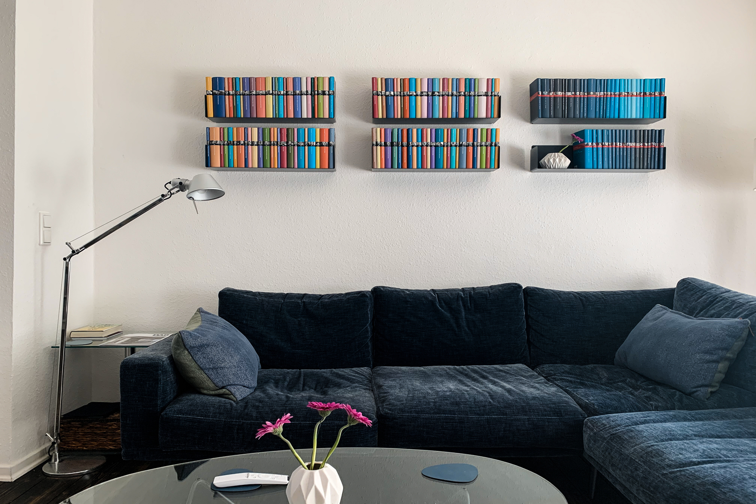 Bibliothèque murale design avec étagères noires et livres colorés au-dessus d’un canapé bleu – inspiration couleur pour bibliothèque murale moderne.